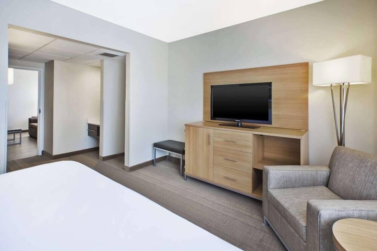 Hotellihuone, jossa on sänky, televisio puukehikossa, sohva ja lamppu.