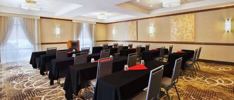 A conference room with tables and chairs, large windows with curtains, and wall-mounted lights.