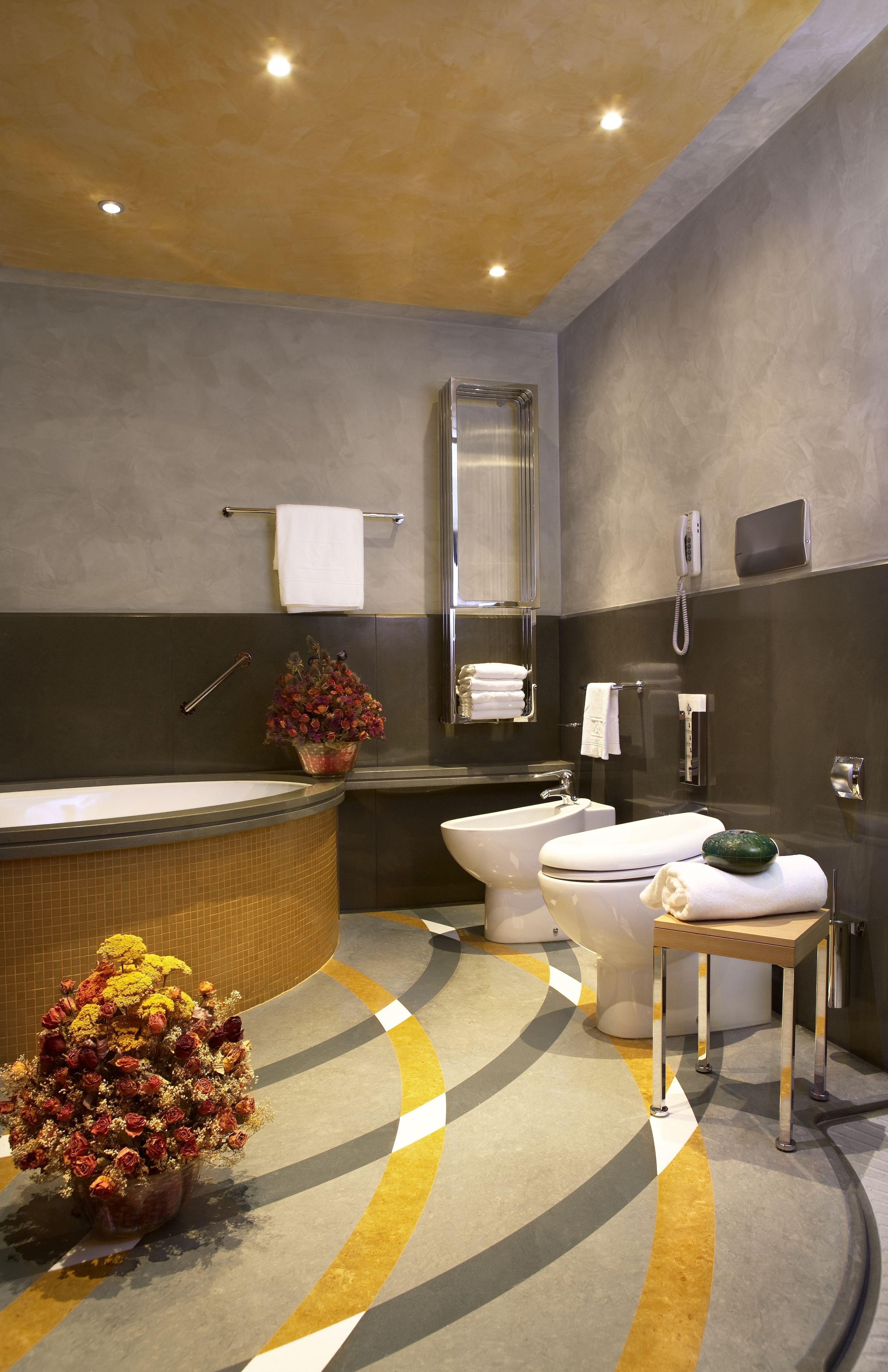 Een moderne badkamer met een bad, toilet en wastafel. Er is een handdoekhouder, een telefoon en een klein tafeltje met een plantje.