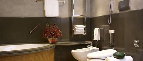 Een moderne badkamer met een bad, toilet en wastafel. Er is een handdoekhouder, een telefoon en een klein tafeltje met een plantje.