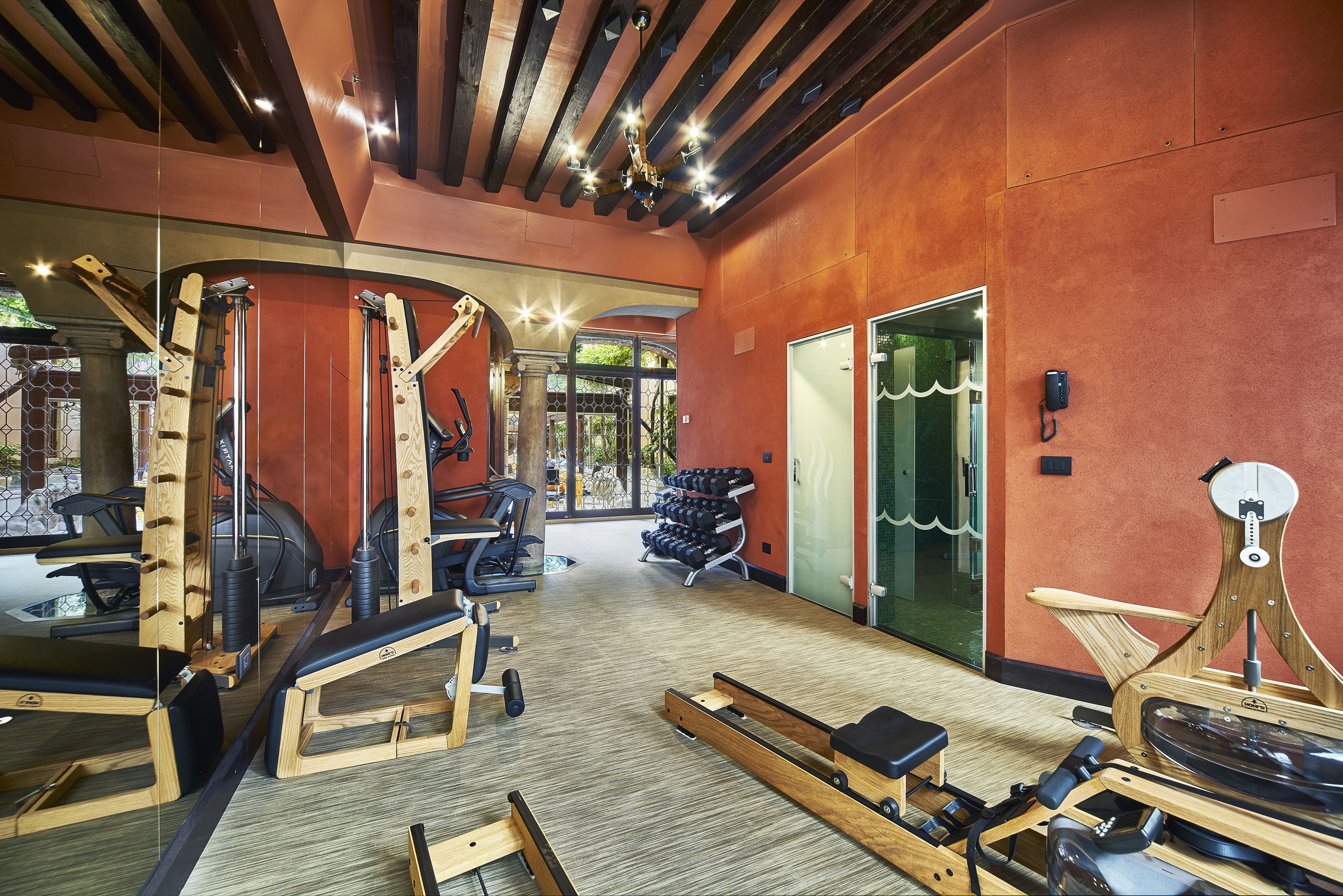 A gym with various exercise equipment, a wooden floor, and a large window providing natural light.