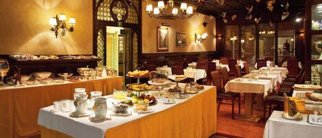 A restaurant with multiple tables, a buffet with various food items, and decorative lighting.