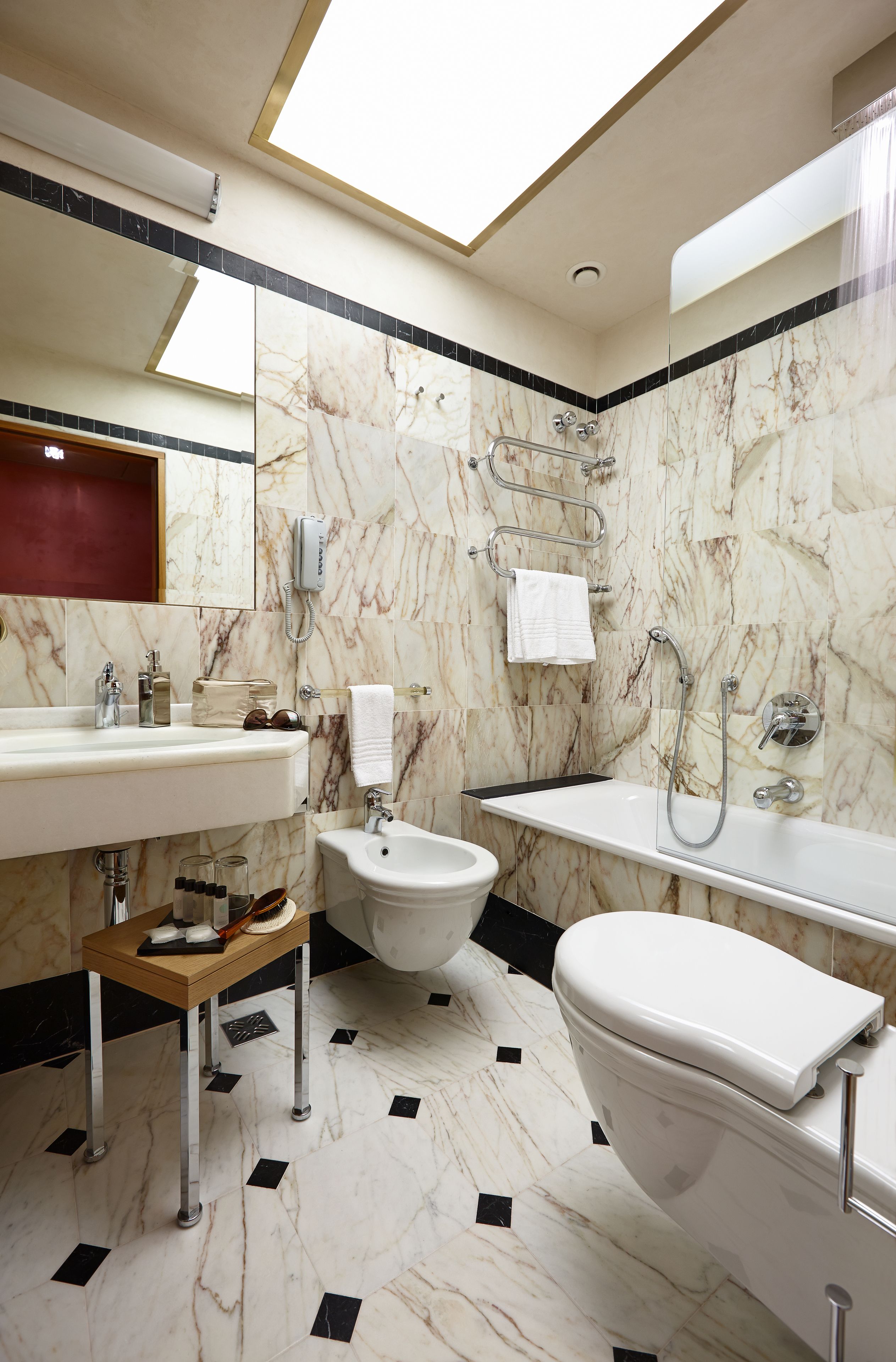 A modern bathroom with a marble floor, a large mirror, a sink, a bidet, and a bathtub.