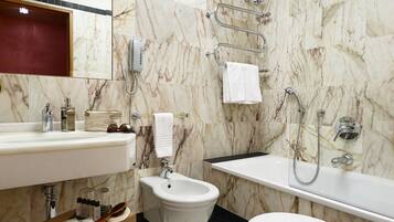 A modern bathroom with a marble floor, a large mirror, a sink, a bidet, and a bathtub.