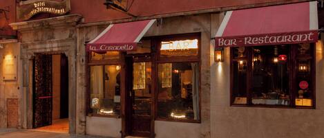 A building with a sign for 'Hotel Caravella' and a 'Bar - Restaurant' with illuminated signage.