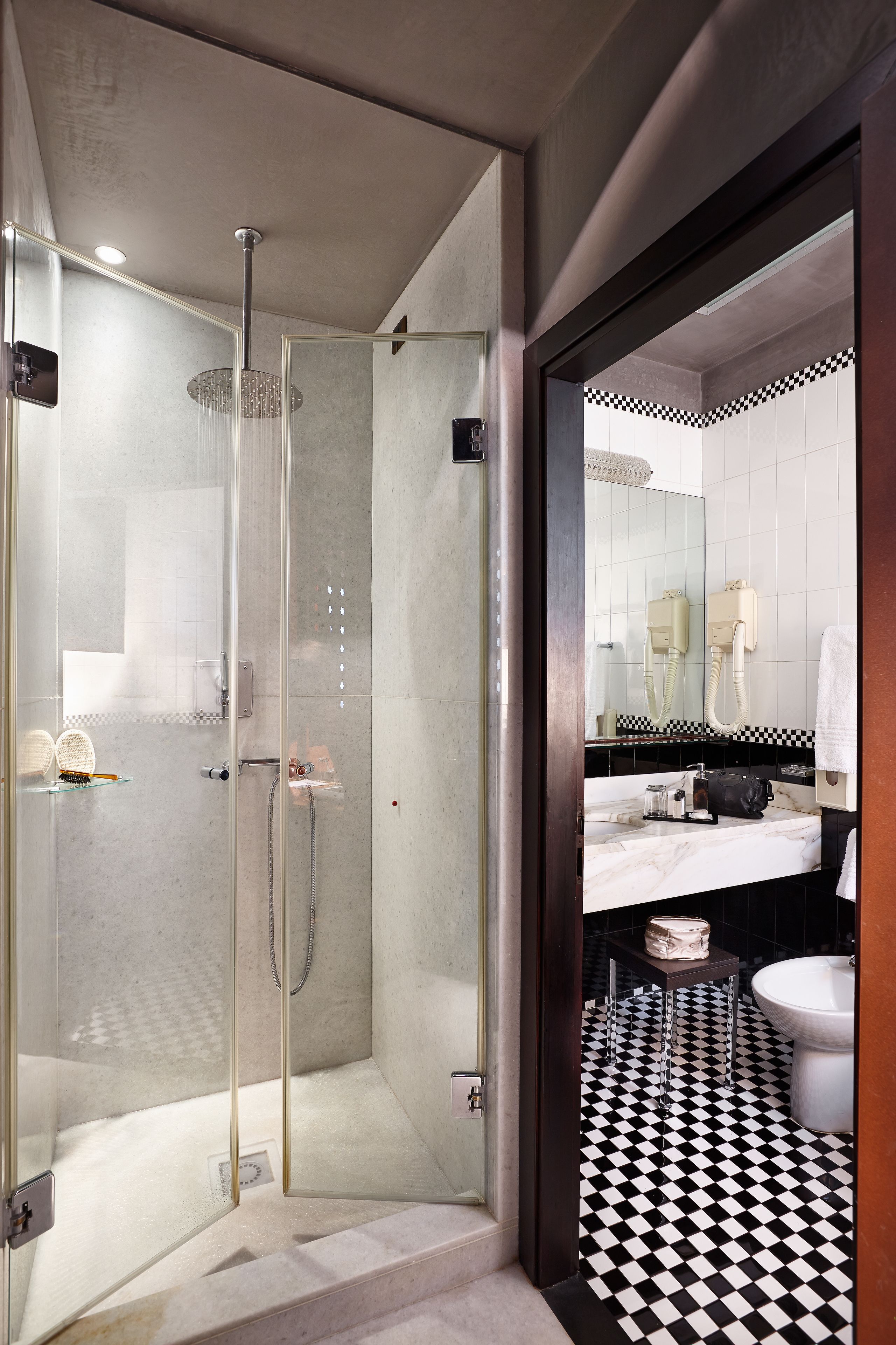 Ein modernes Badezimmer mit einer gläsernen Duschkabine, einem schwarz-weißen Schachbrettboden und einem weißen Waschbecken.