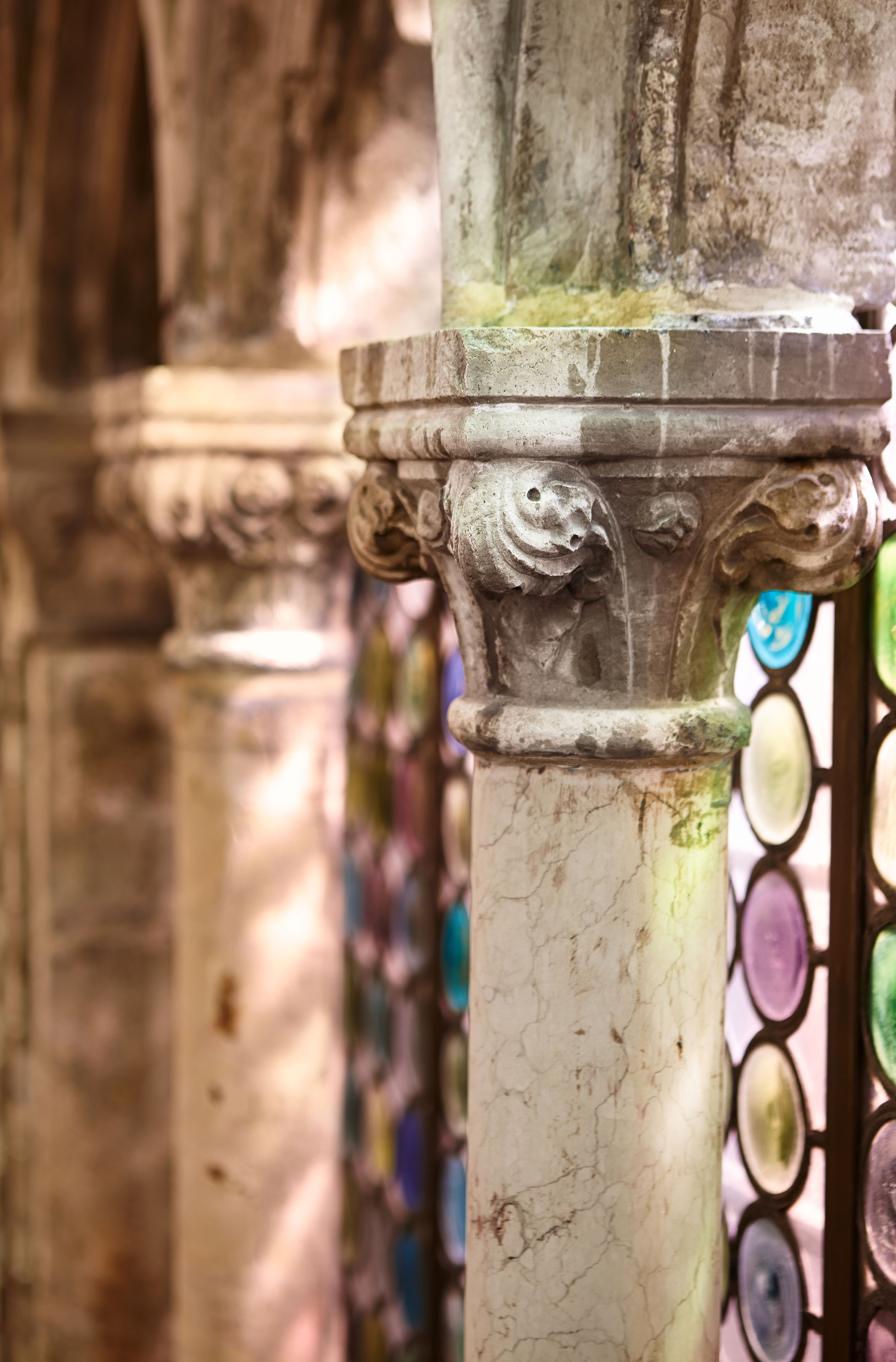 A close-up of a weathered column with intricate carvings, part of a larger structure with a stained glass window in the background.