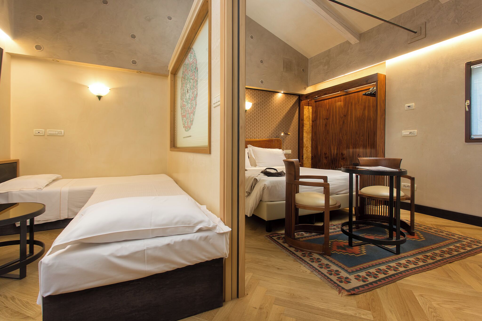 Habitación de hotel con dos camas, una mesita, una silla y una alfombra.