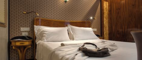 A neatly made bed with white linens, a wooden headboard, a bedside table with a lamp, and a wall with a patterned wallpaper.