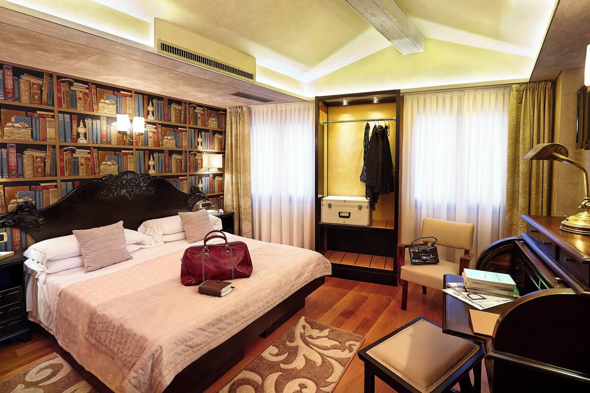 Una habitación de hotel con una cama grande, una estantería, un escritorio y una silla.