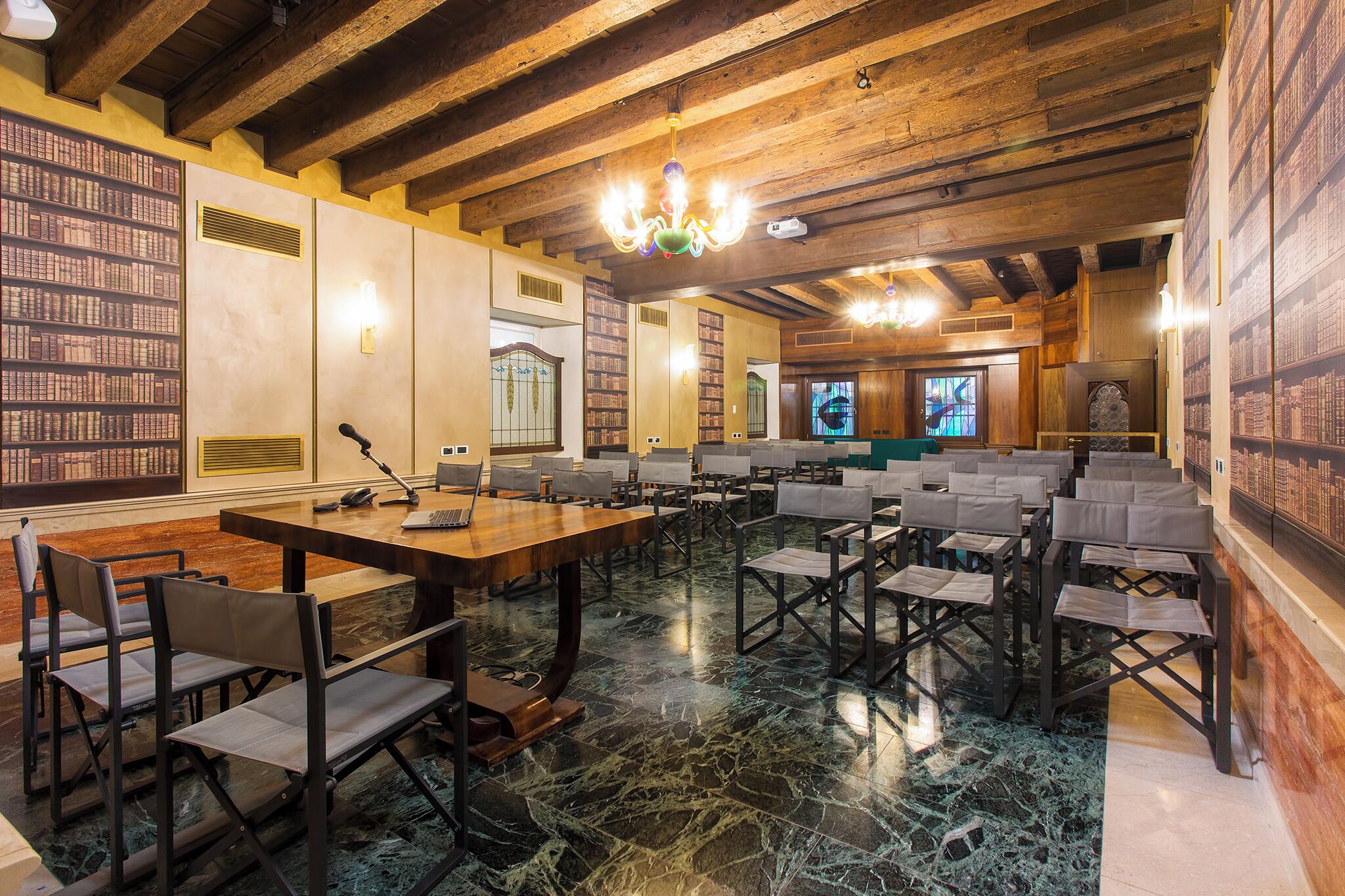 A spacious library with wooden beams, a marble floor, and rows of bookshelves.