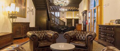 A luxurious lobby with leather sofas, a round table, a chandelier, and a staircase.