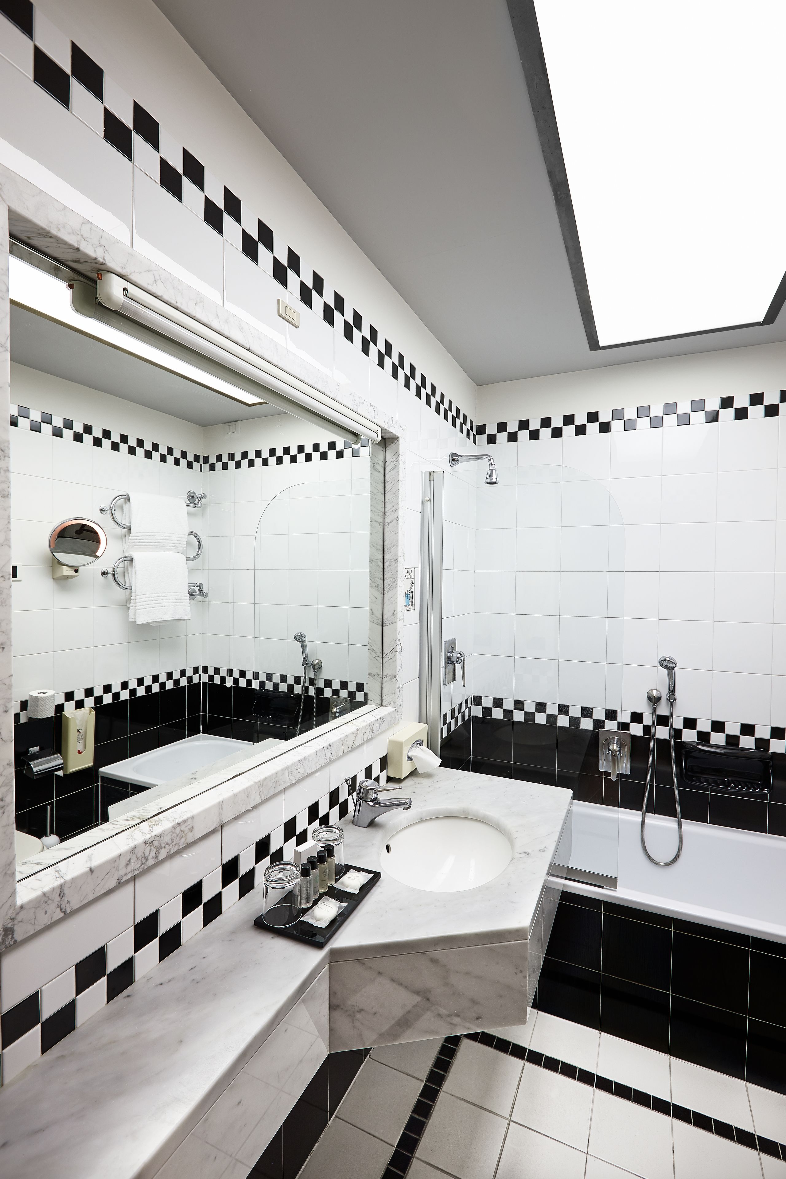 A modern bathroom with a large mirror, two sinks, a shower, and black and white checkered tiles.