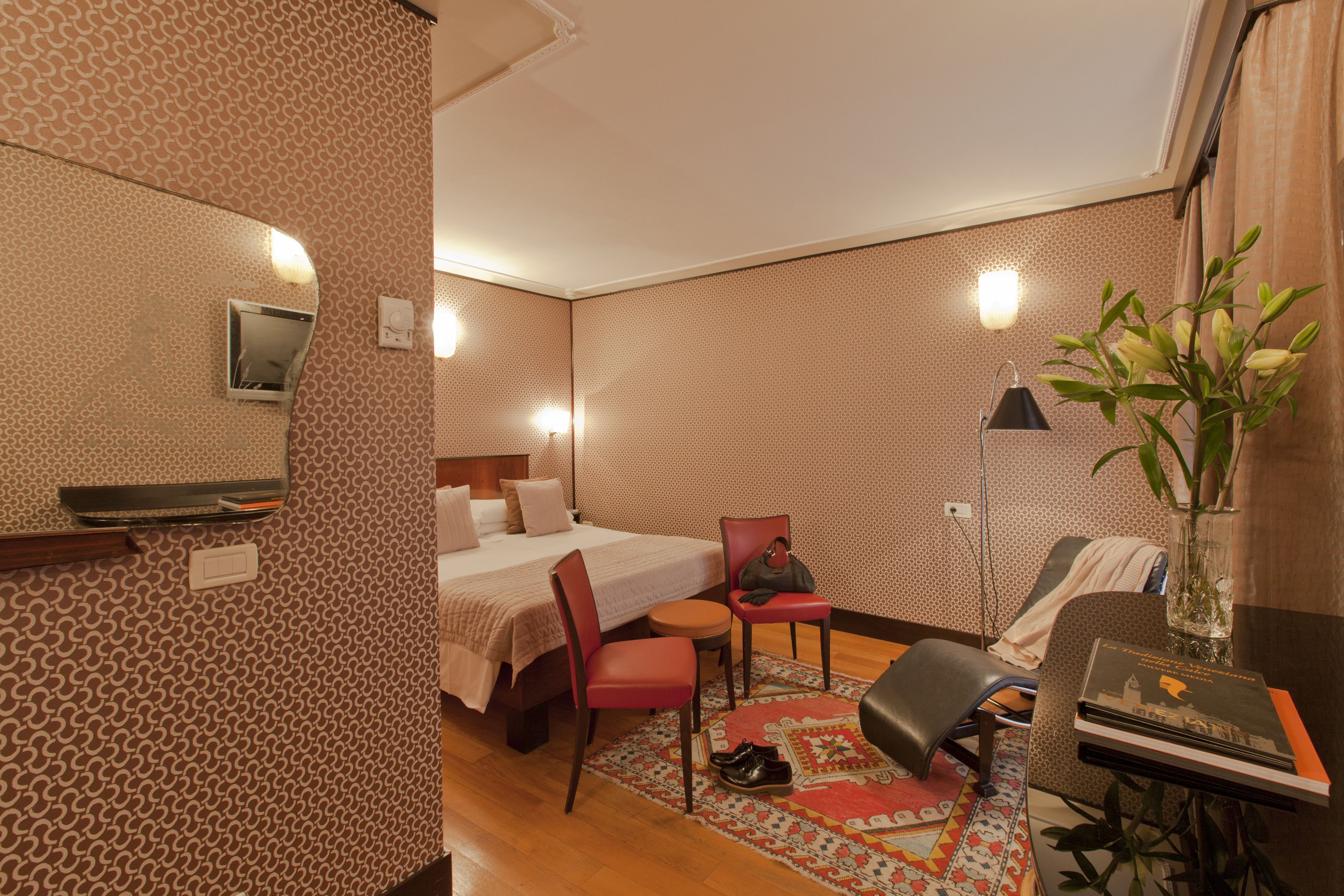 Una habitación de hotel con cama, escritorio, silla, una mesita, espejo y planta.