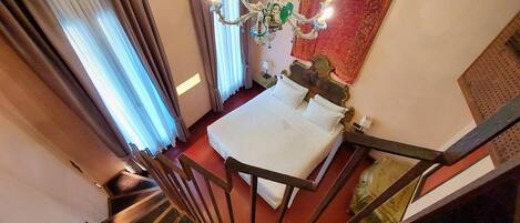 Un dormitorio con cama, una araña, cortinas, una alfombra roja y una escalera.