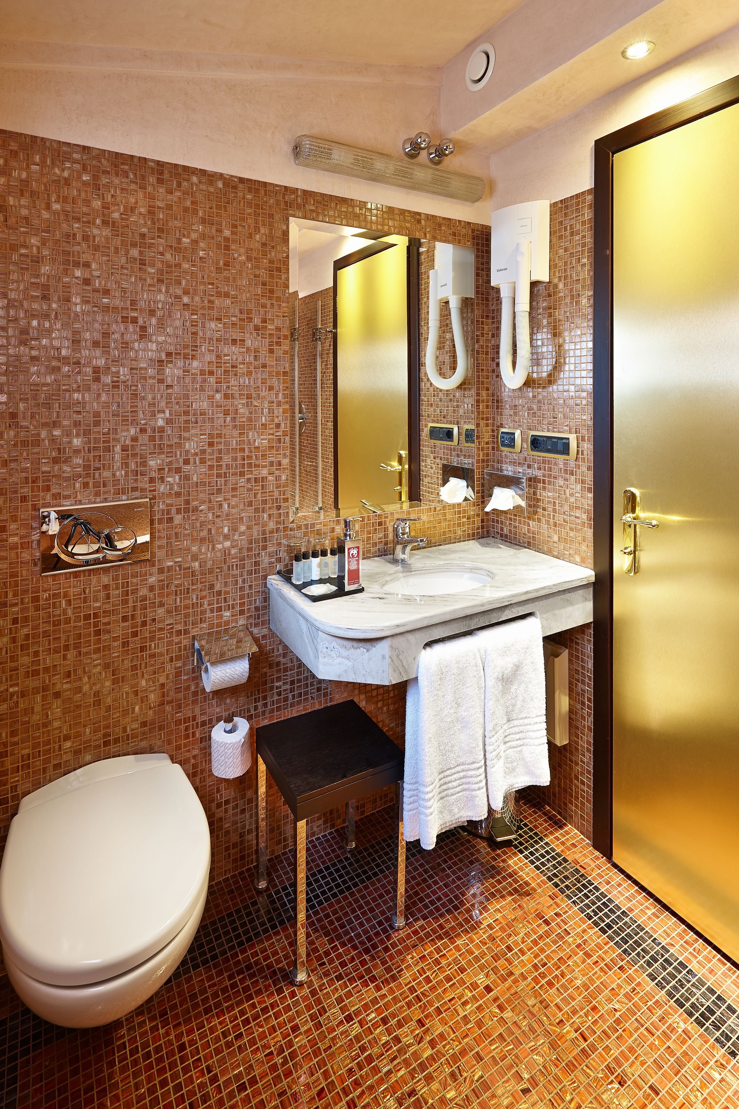 Un bagno con pavimento piastrellato, un lavandino, un water e uno specchio.