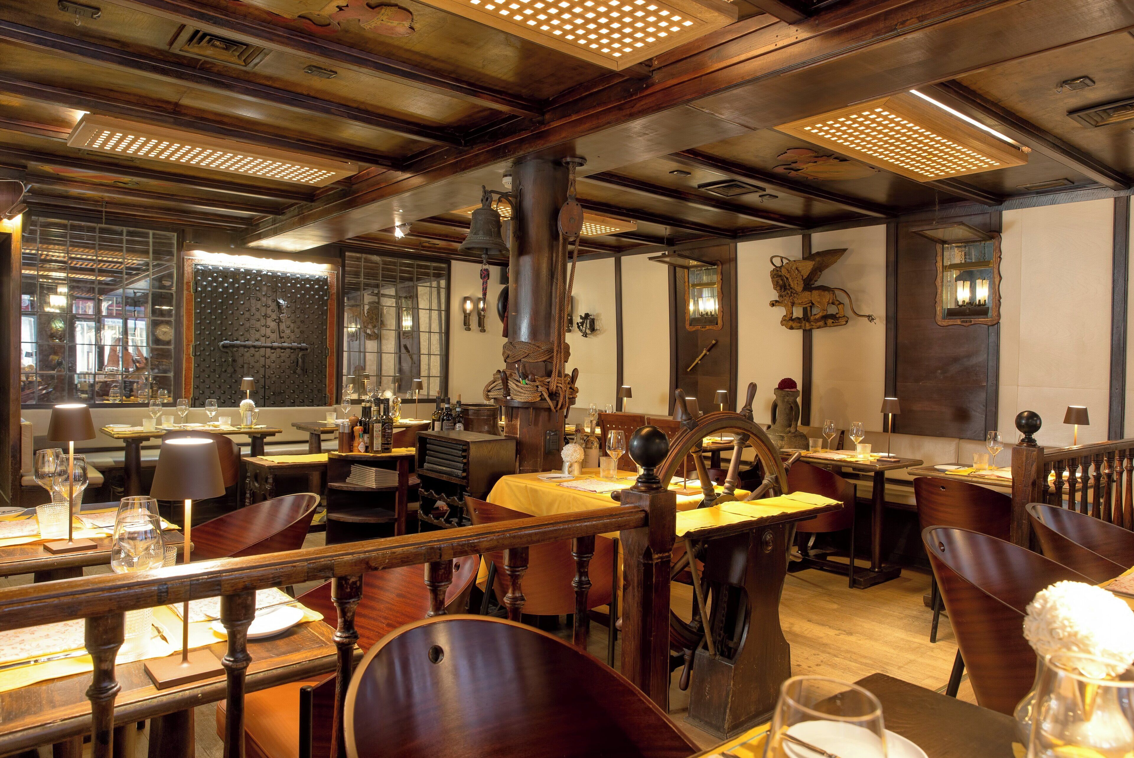A restaurant interior with wooden furniture, tables set with wine glasses, and a large decorative bell.