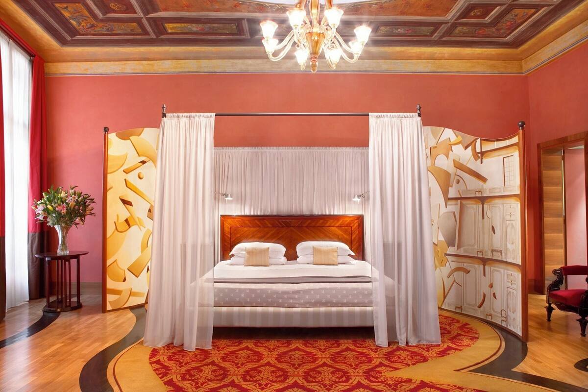 Una cama grande con cabecera de madera, ropa de cama blanca y cortinas traslúcidas.