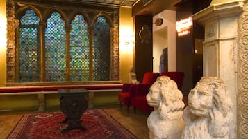 Ein Zimmer mit einem großen Buntglasfenster, einem roten Sessel und zwei steinernen Löwenstatuen.