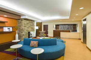 Un espacio de sala moderno con un sofá azul, mesas redondas blancas, un muro de acento de piedra y una cocina al fondo.