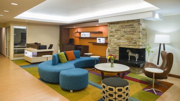 A modern lounge area with a blue sofa, ottomans, a fireplace, a stone wall, and a reception desk. - Best Western Allentown Bethlehem Lehigh Valley Inn & Suites (Bethlehem)