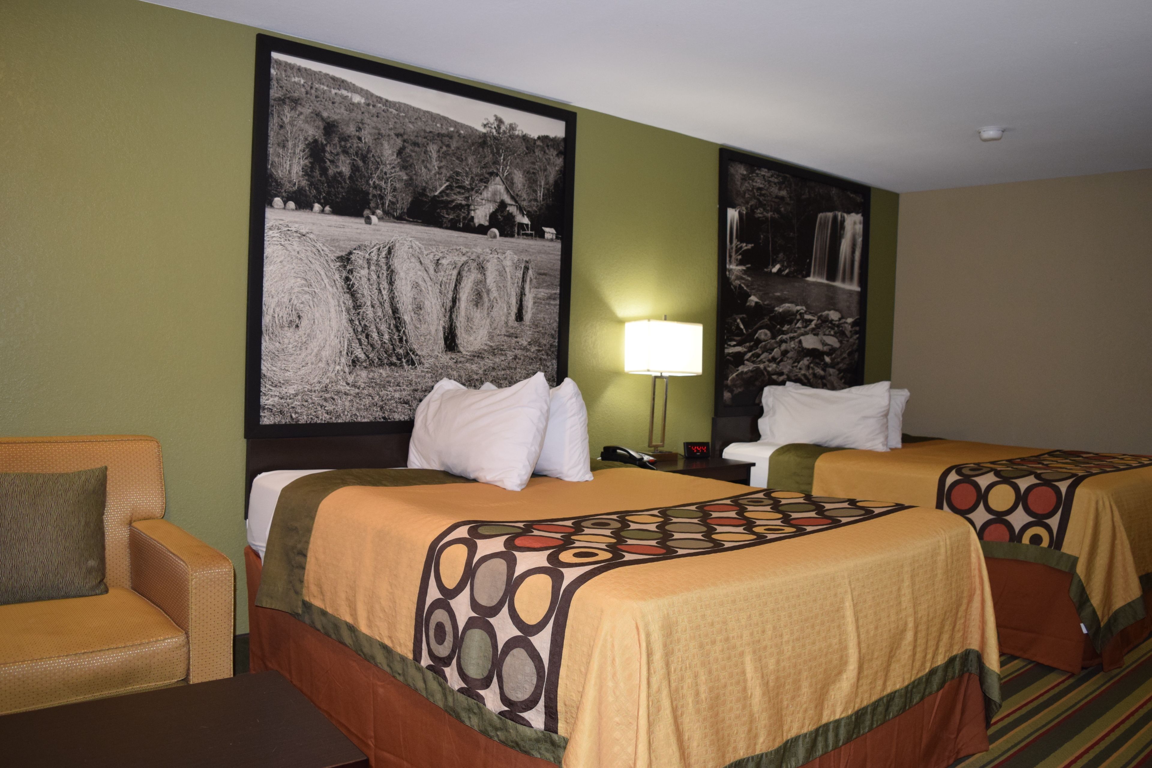 A hotel room with two beds, a sofa, a lamp, and a large black and white landscape painting on the wall.