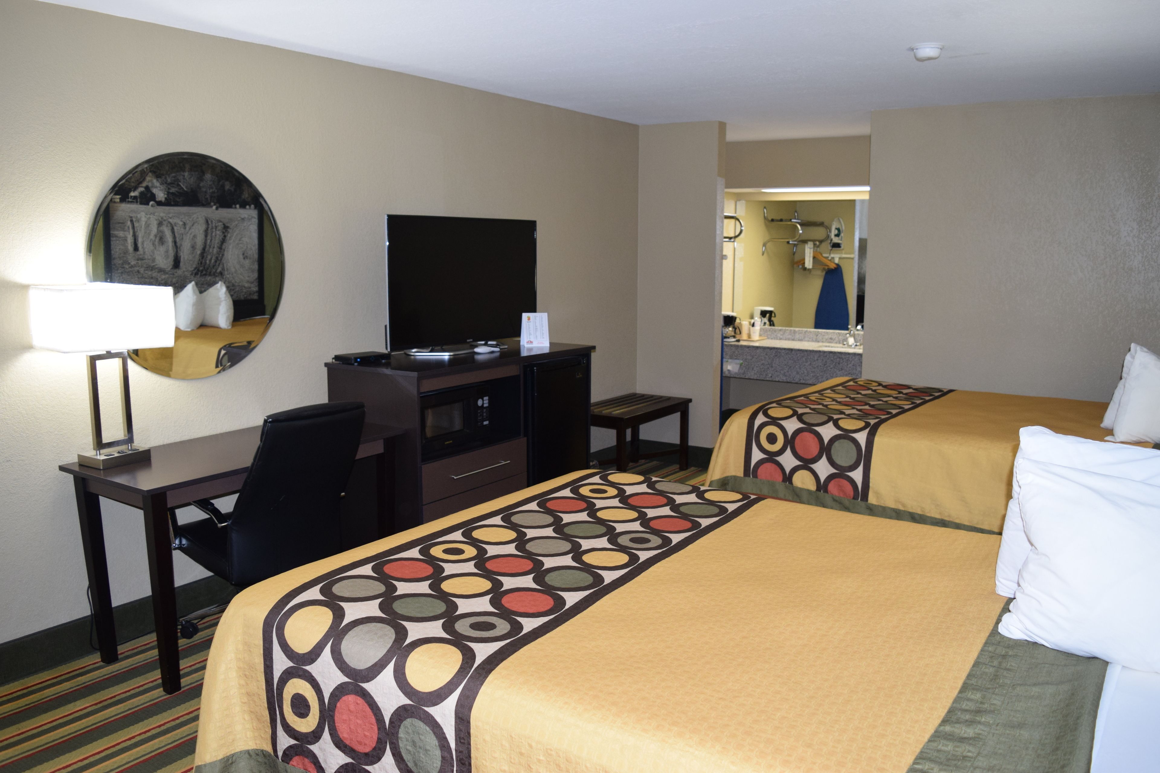 A hotel room with two beds, a desk, a chair, a television, and a bathroom visible through an open door.