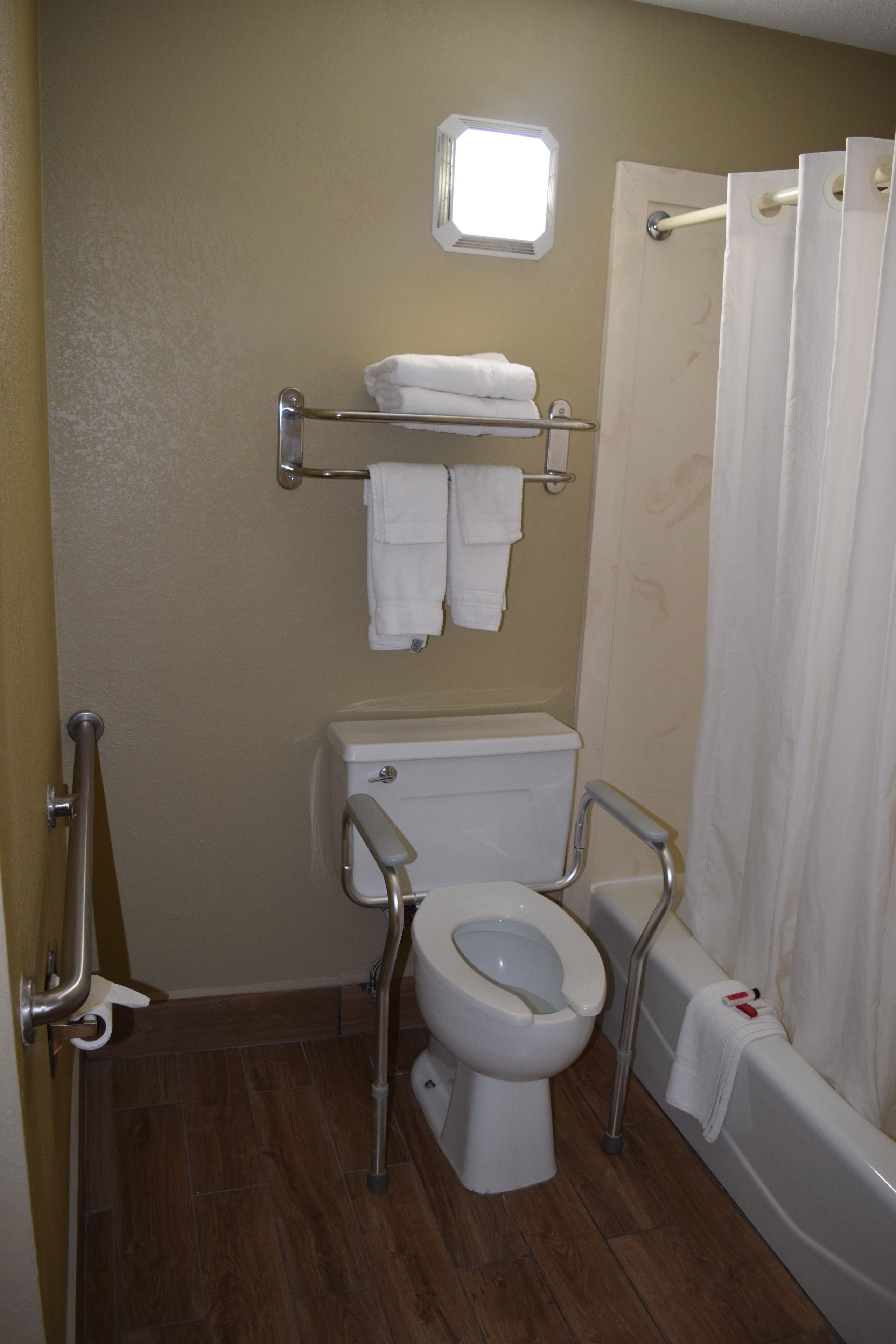 A bathroom with a toilet, grab bars, a shower curtain, and a towel rack.