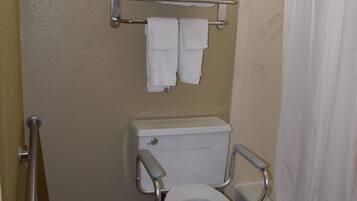 A bathroom with a toilet, grab bars, a shower curtain, and a towel rack.