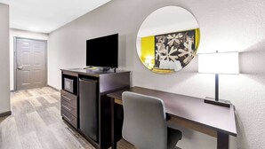 Una habitación de hotel con escritorio, televisor de pantalla plana, espejo y lámpara.