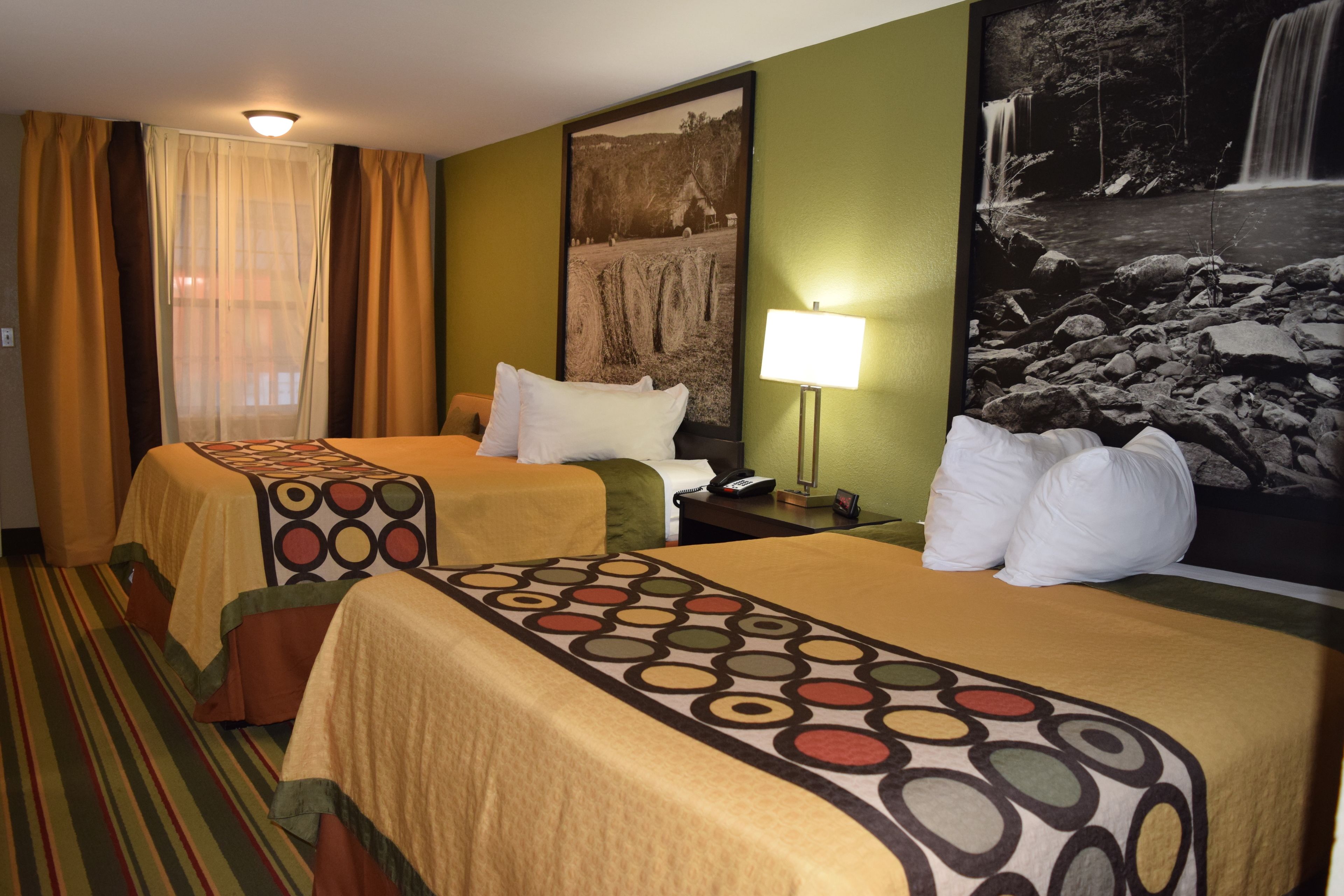 Habitación de hotel con dos camas, un ventanal con cortinas, una lámpara de pared y un cuadro con una cascada.