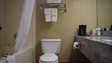 Casa de banho com sanita, um porta-toalhas com toalhas dobradas, máquina de café e dispensador de papel.