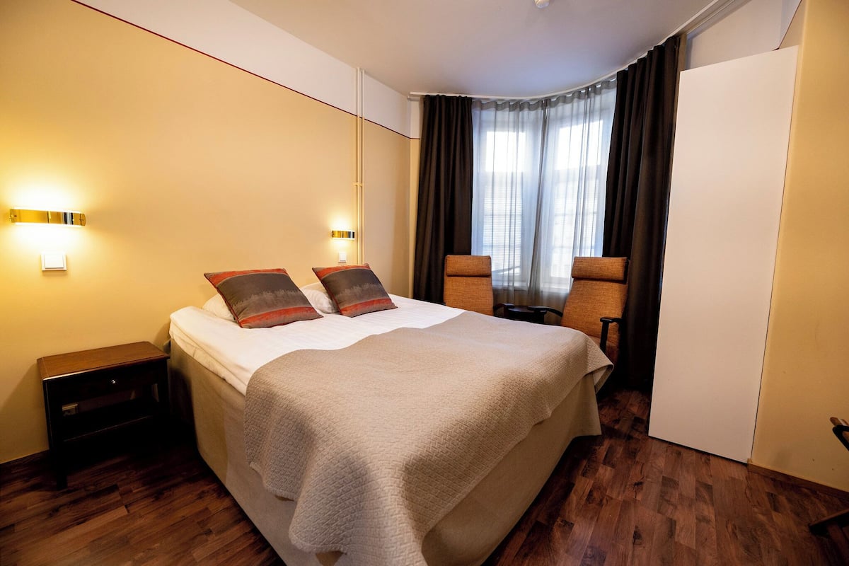 A hotel room with a bed, bedside tables, a chair, and a wardrobe.