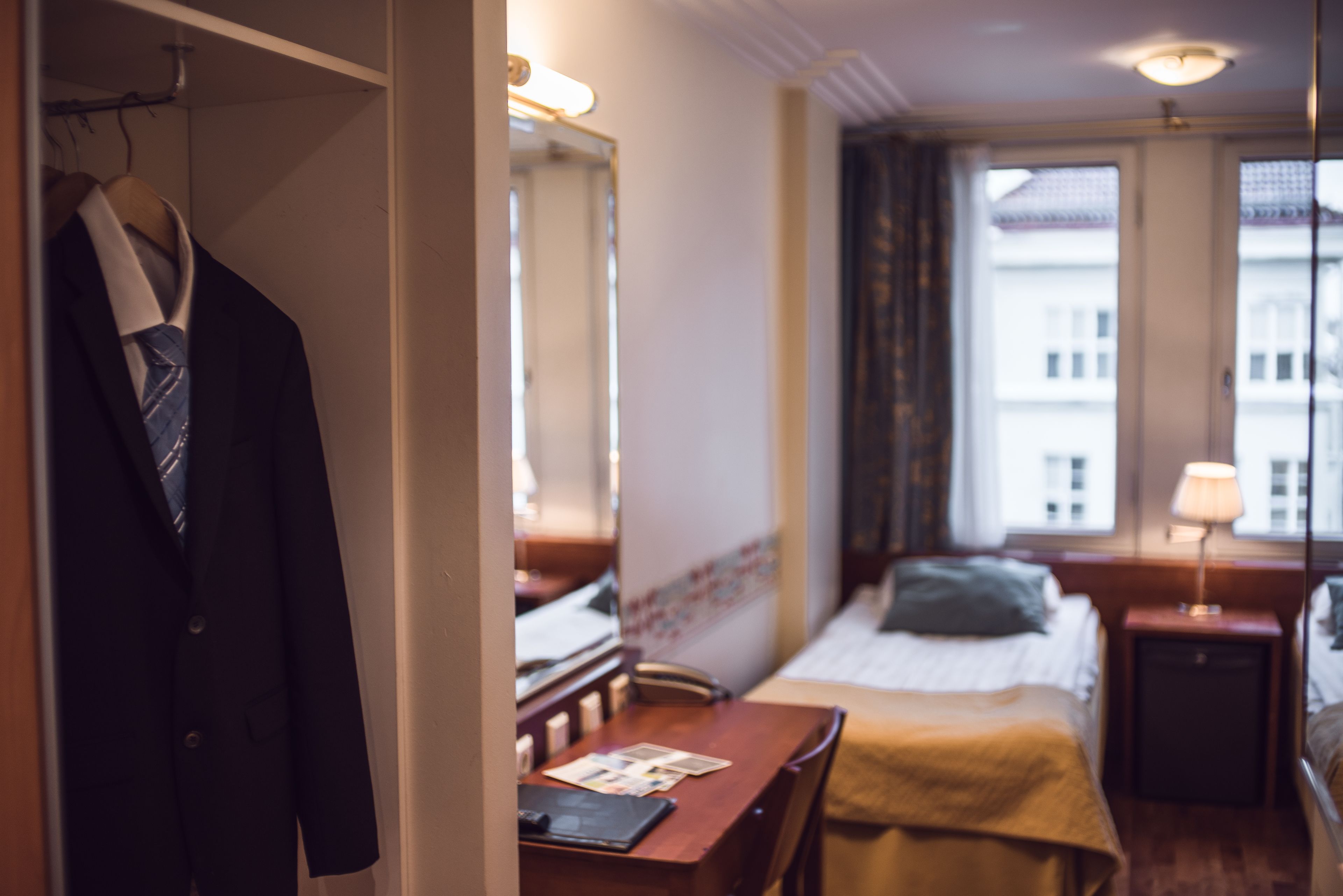Habitación de hotel con cama, escritorio, silla, armario y ventana con cortinas.