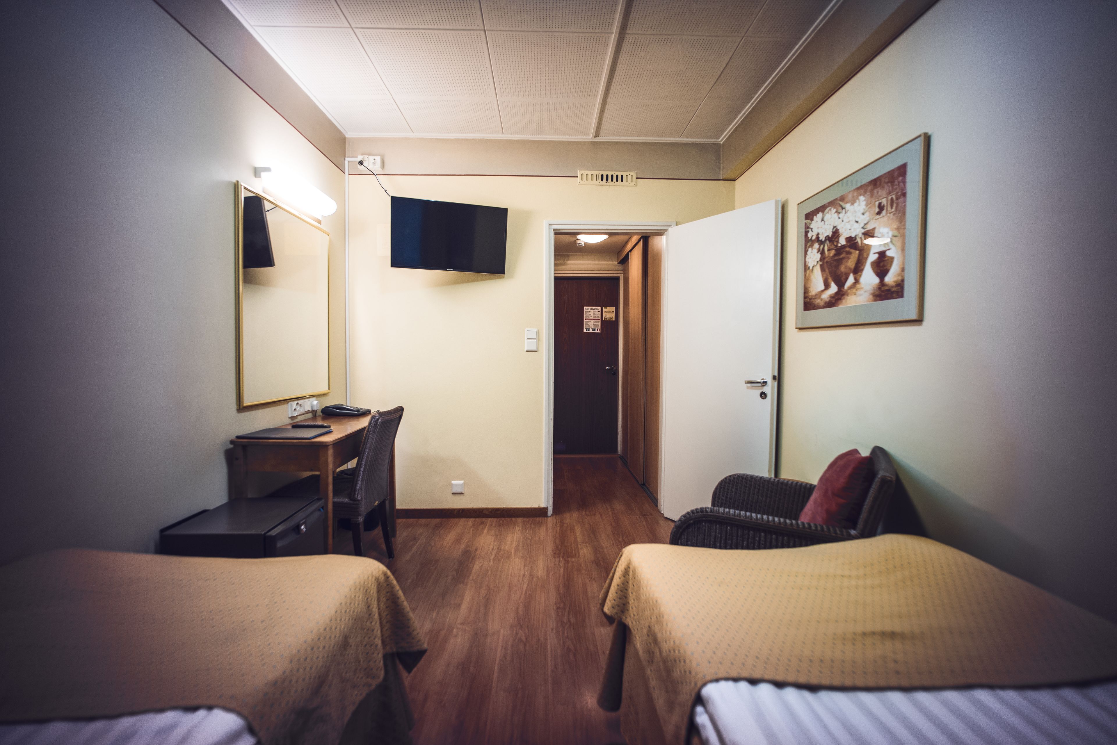 Habitación de hotel con dos camas, un escritorio, una silla, un televisor y una puerta que da a otra habitación.