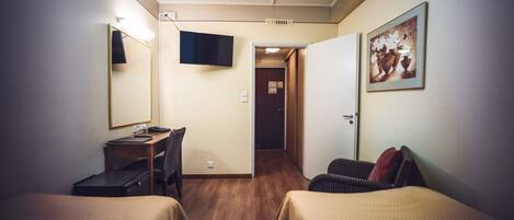 Habitación de hotel con dos camas, un escritorio, una silla, un televisor y una puerta que da a otra habitación.