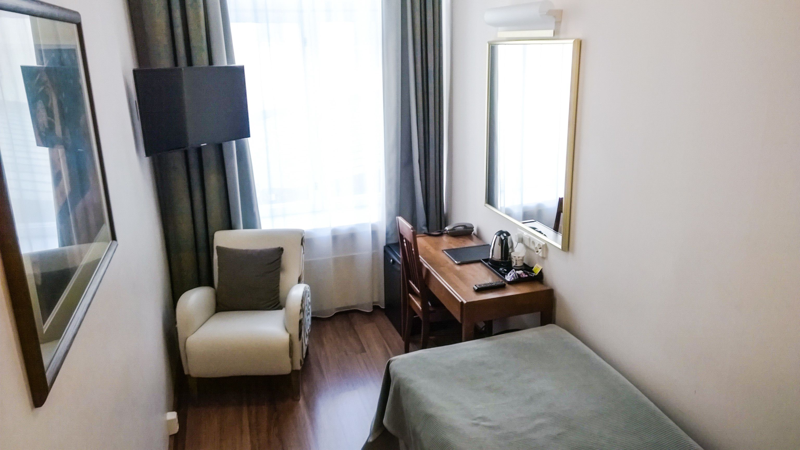 A hotel room with a bed, a desk with a chair, a television, and a window with curtains.