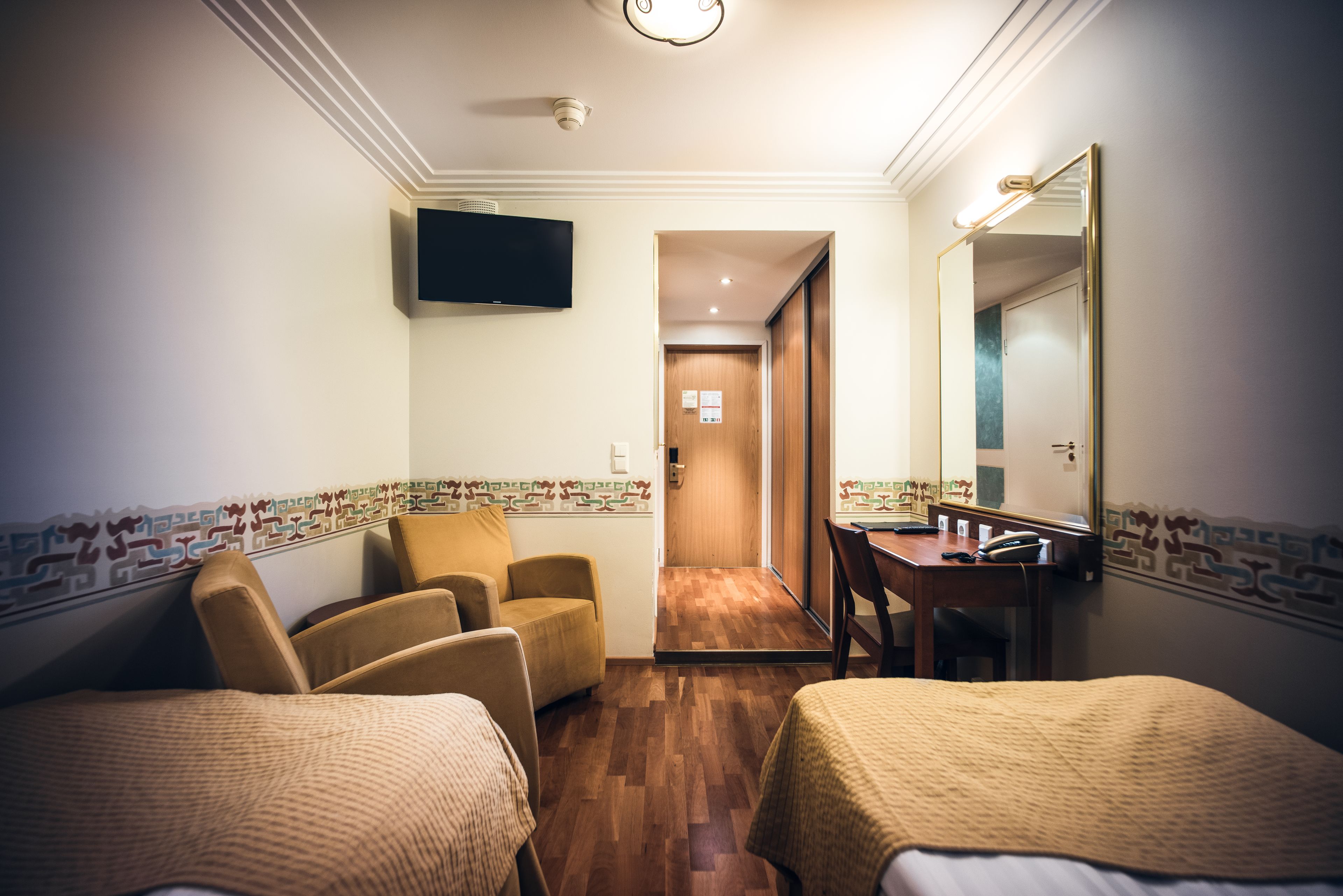 A hotel room with two beds, a desk, a chair, a television, and a door leading to another room.