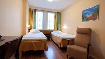Quarto de hotel com duas camas de solteiro, uma escrivaninha de madeira, uma cadeira, uma janela com cortinas e um quadro na parede.