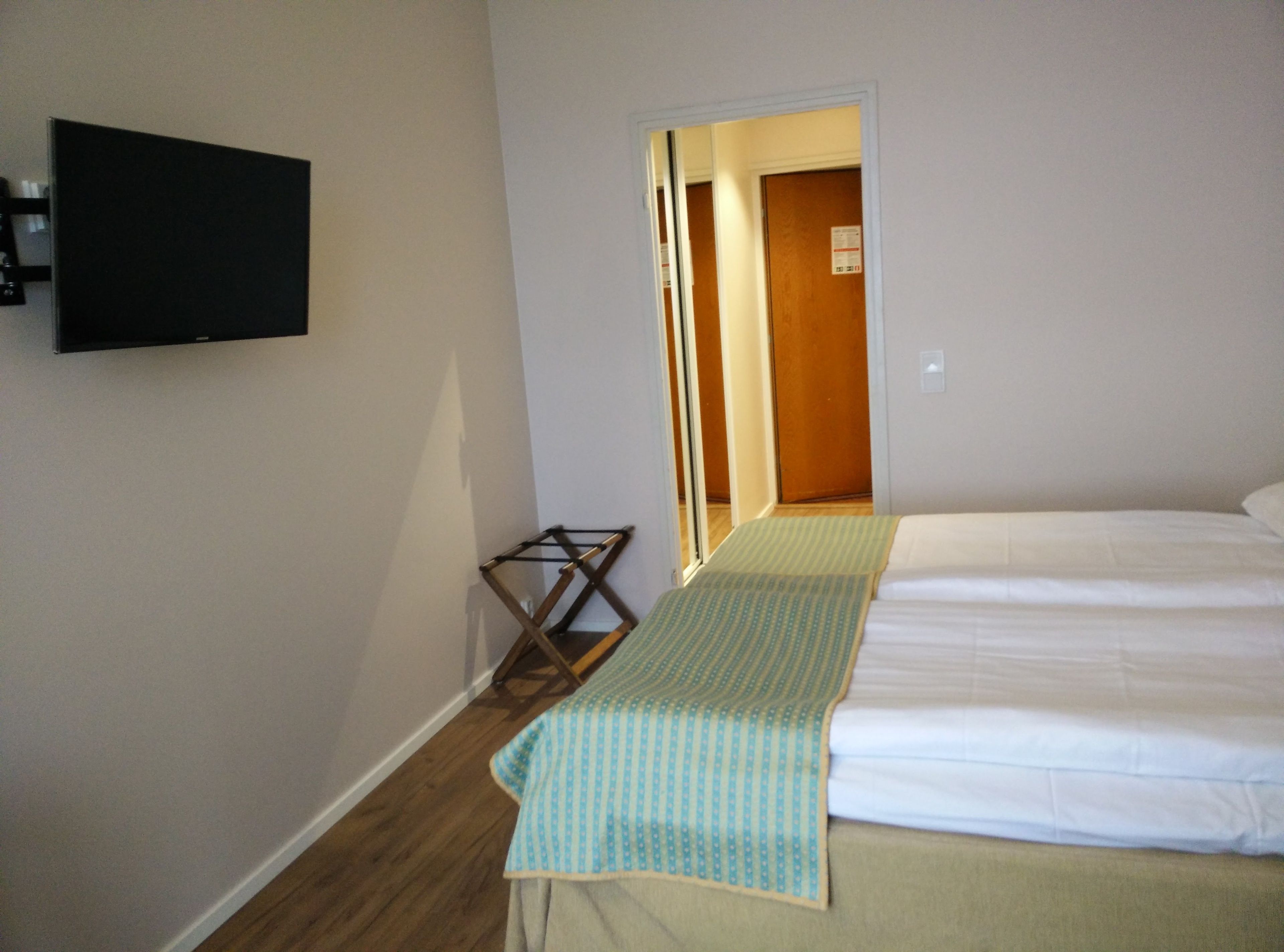 Ein Hotelzimmer mit einem Bett, einem an der Wand montierten Fernseher und einem Holzstuhl.
