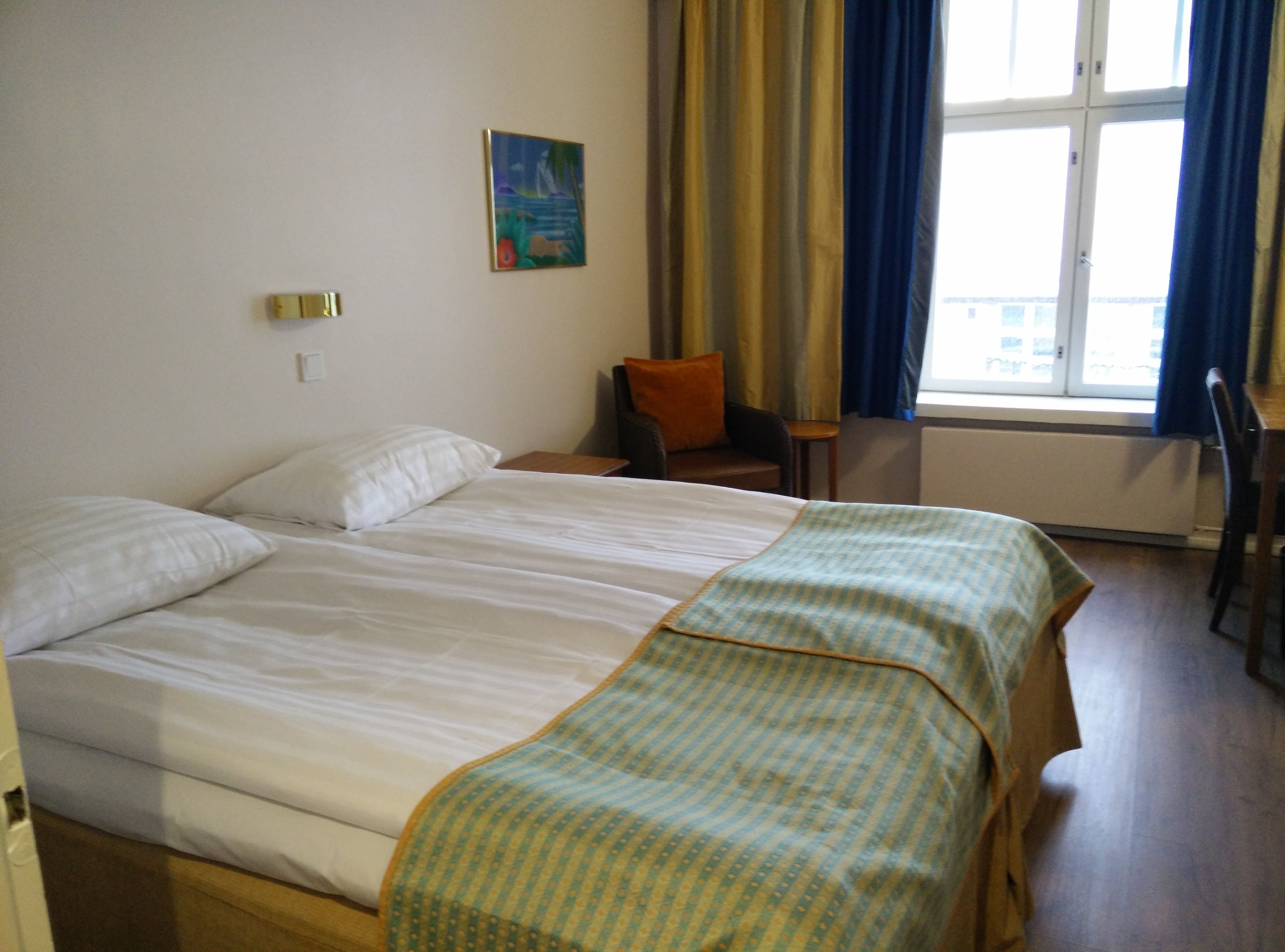 A hotel room with a large bed, a chair, a small table, and a window with curtains.