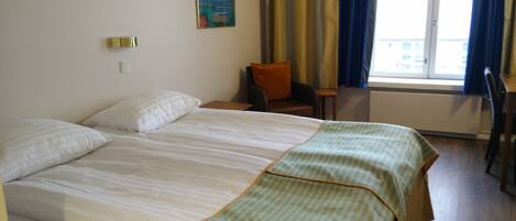 A hotel room with a large bed, a chair, a small table, and a window with curtains.