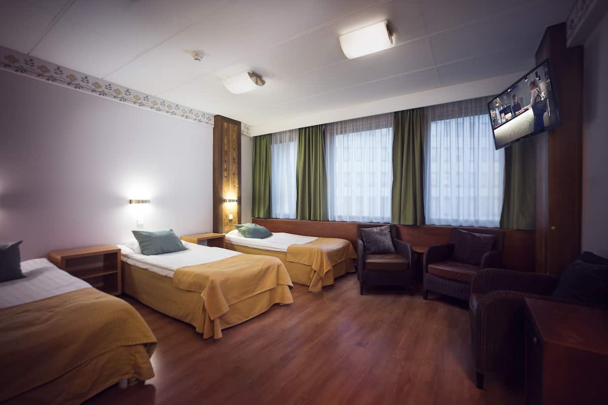 Hotellihuone, jossa on kaksi erillistä sänkyä, sohva, televisio ja ikkuna, jossa on verhot.