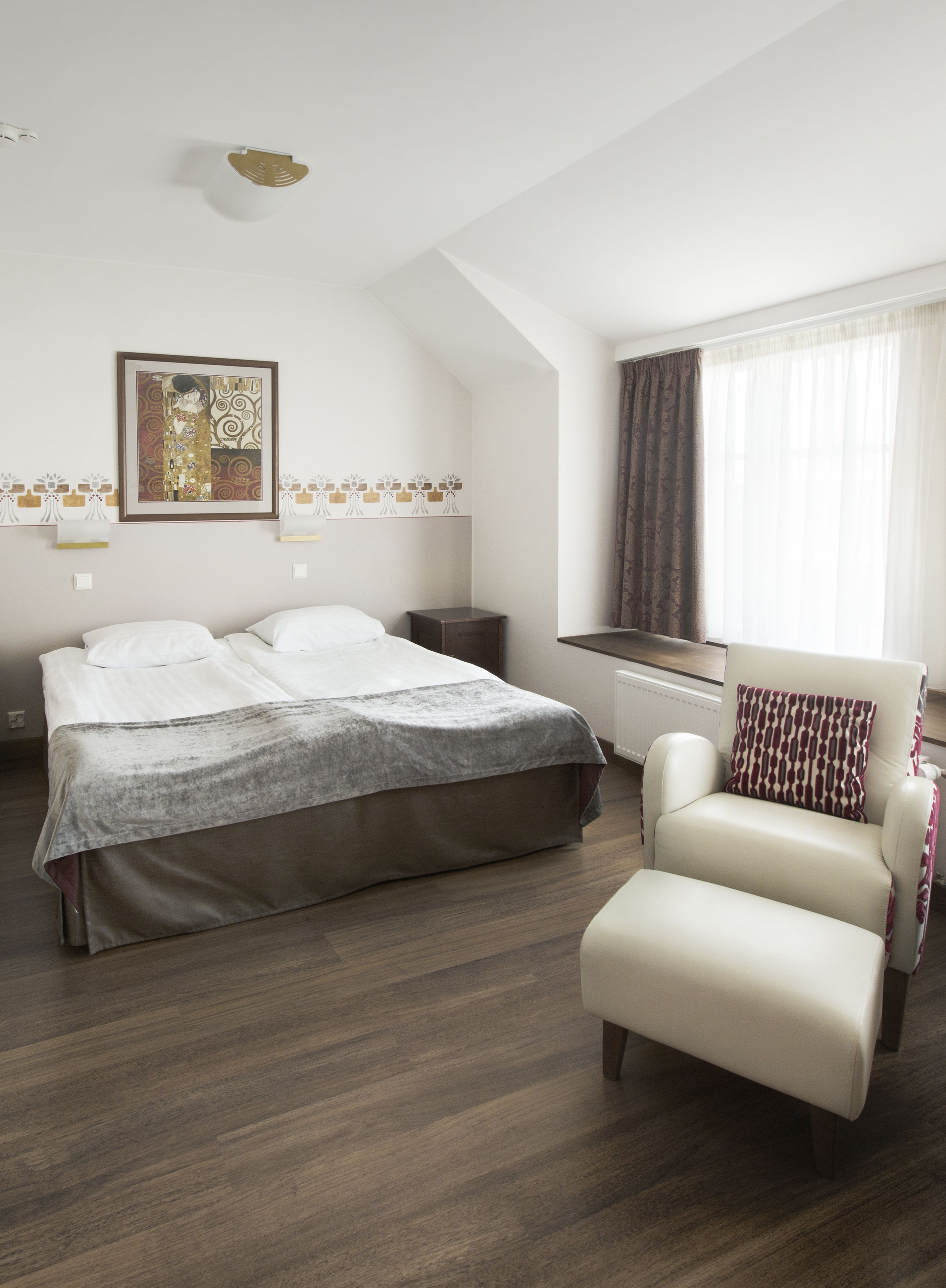 Un dormitorio con cama, una silla, un radiador y una ventana con cortinas.