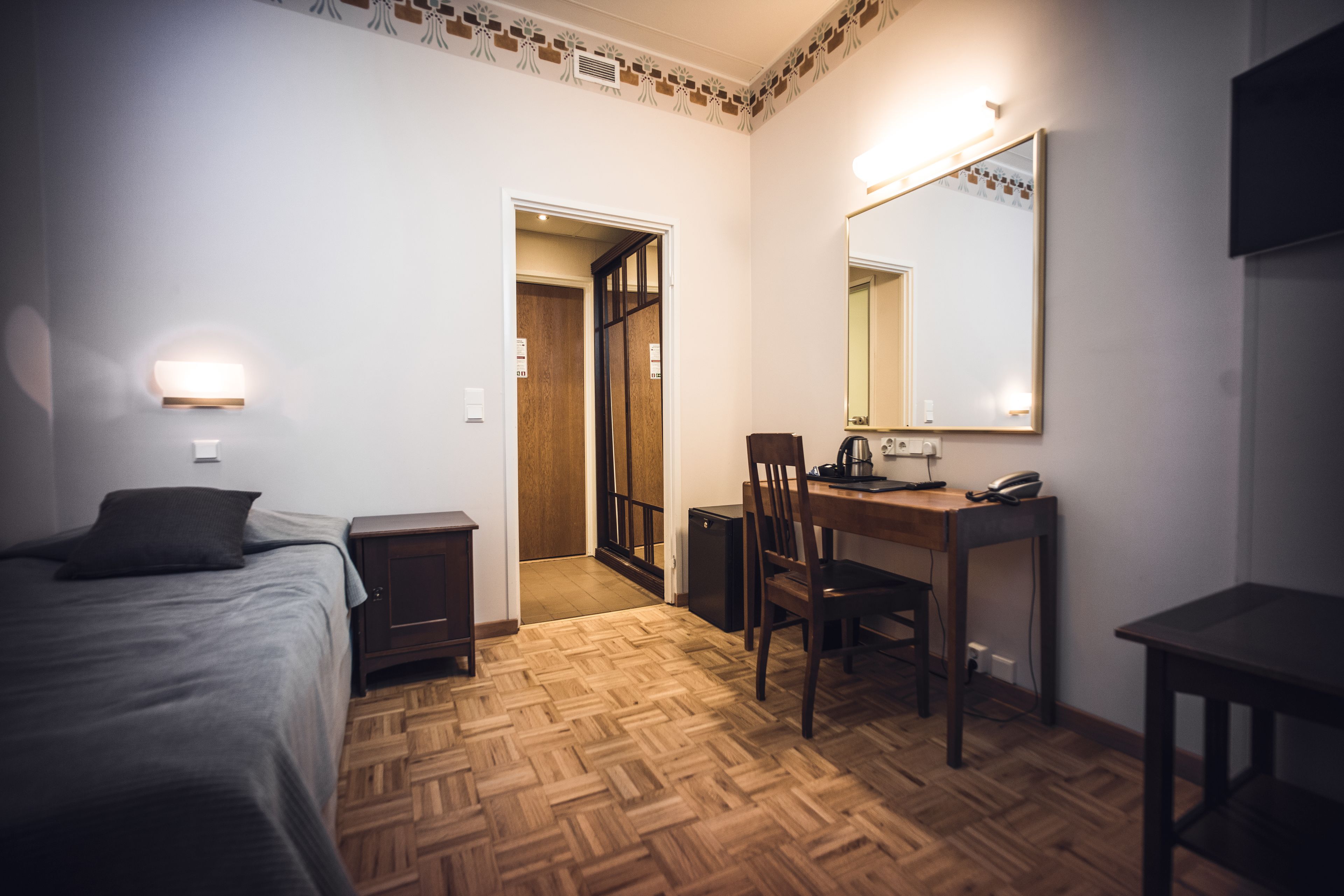 A hotel room with a bed, a desk with a chair, a mirror, and a small table.