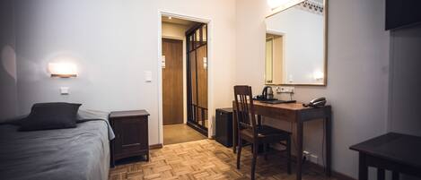 A hotel room with a bed, a desk with a chair, a mirror, and a small table.