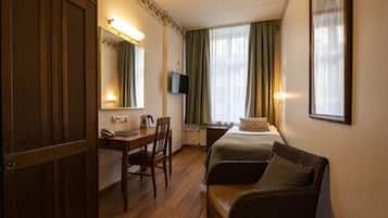 Ein Hotelzimmer mit einem Bett, einem Schreibtisch mit Telefon, einem Sessel, einem an der Wand befestigten Fernseher und einem Fenster mit Vorhängen.