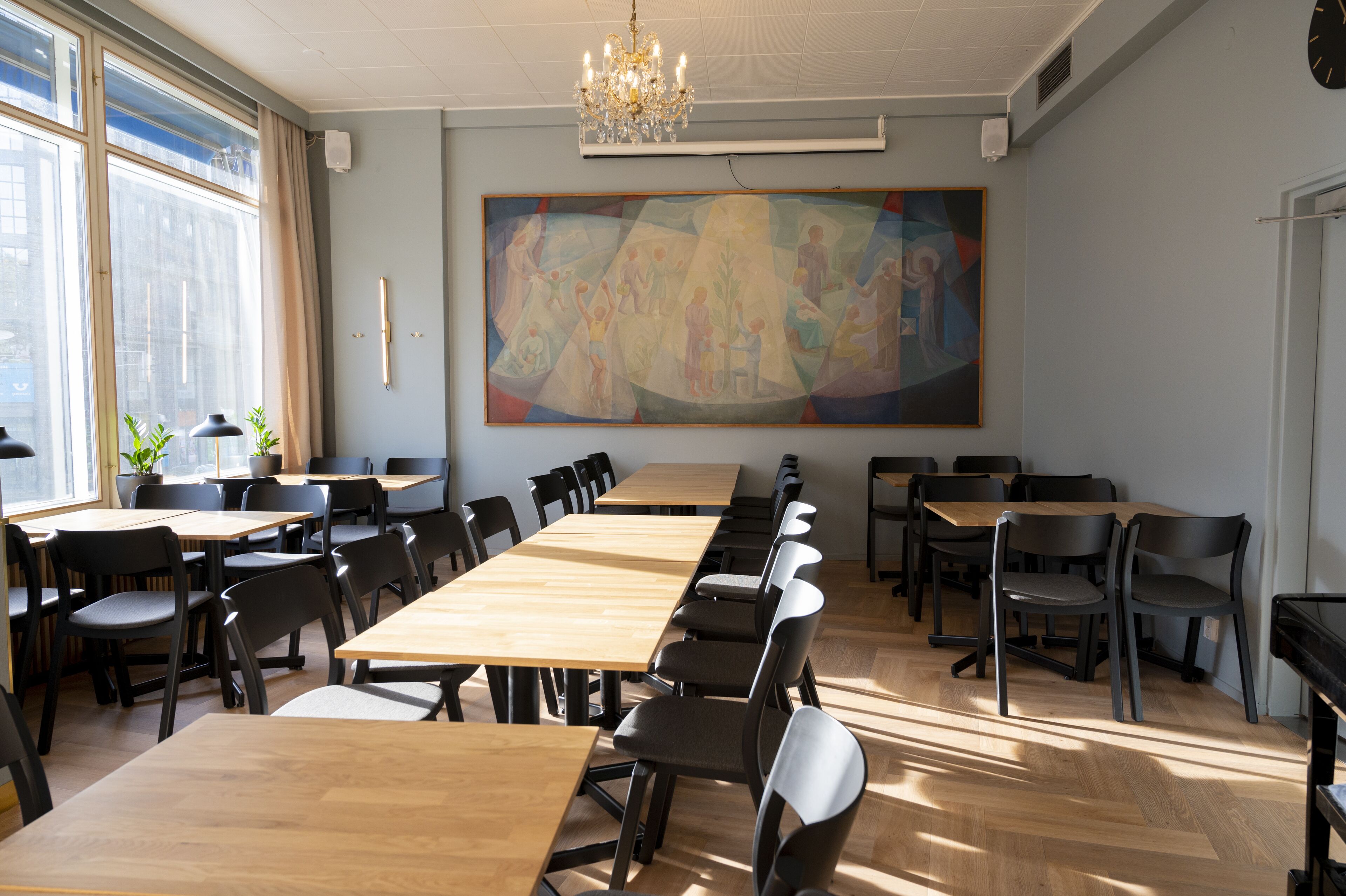 A conference room with long tables and chairs, a large abstract painting on the wall, and a chandelier.