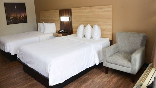 Een hotelkamer met twee bedden, een grijze fauteuil, een nachtkastje met een telefoon, en een stadsgezicht op de muur.