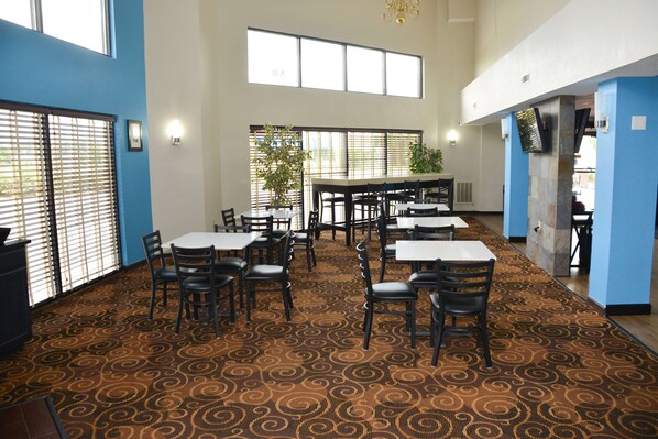 Un comedor amplio con varias mesas y sillas, ventanas grandes y una alfombra estampada.